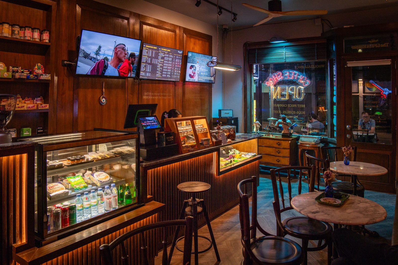 Inside The Grasshopper: wood-panelled room, glass display counter, TV menus above the bar and café tables
