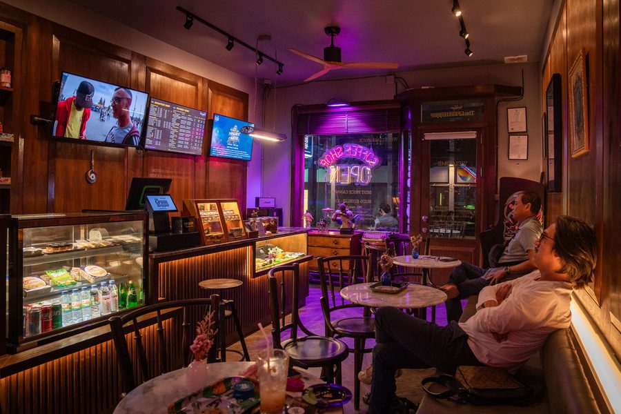 Guests relaxing at café tables under the TV menus and purple neon